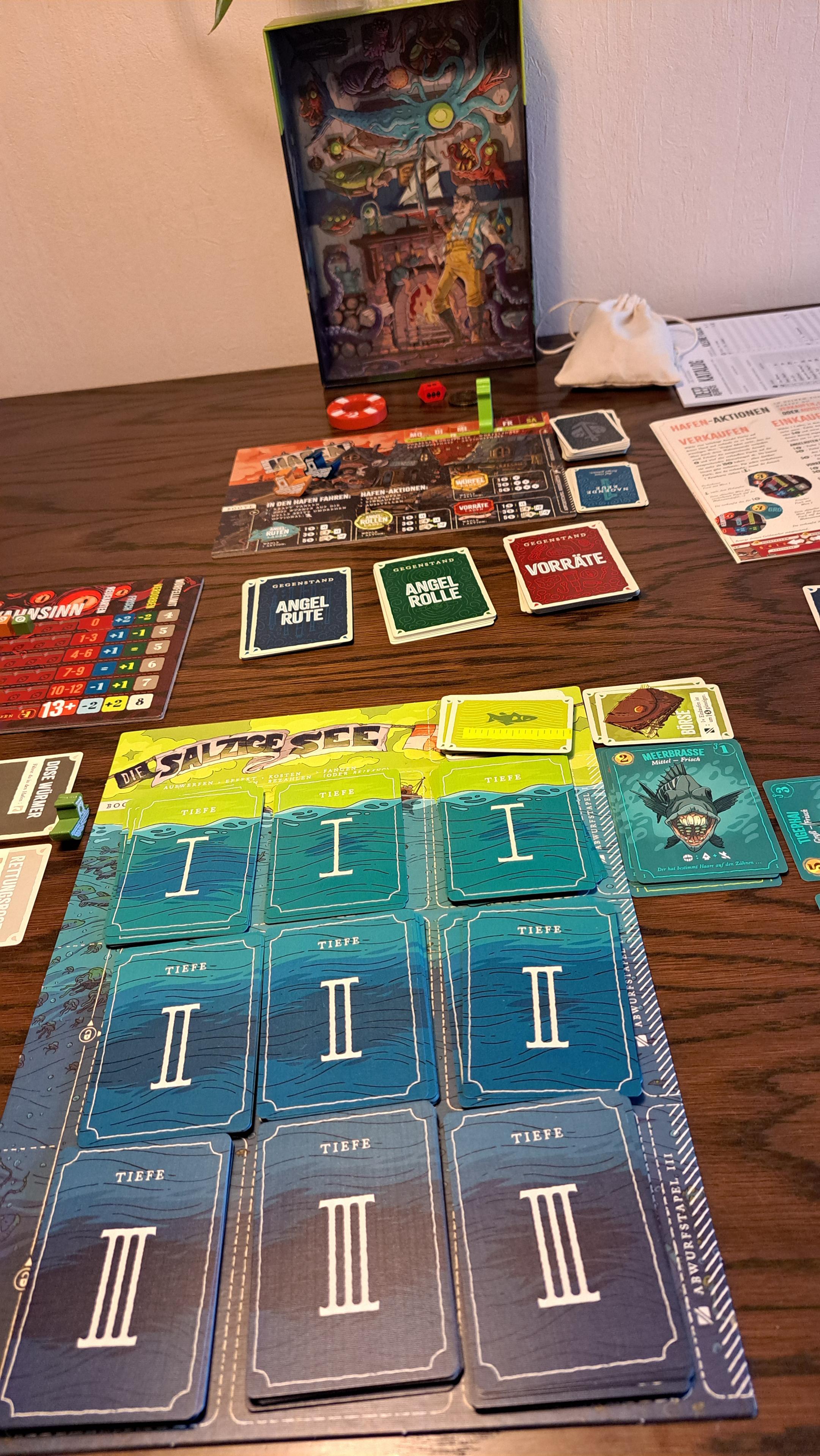 The sea board with 3 regions (depths), and 3 piles of cards for each. In the background: the harbour board and some piles of gear cards, and the game box lid with really cool artwork on the inside!