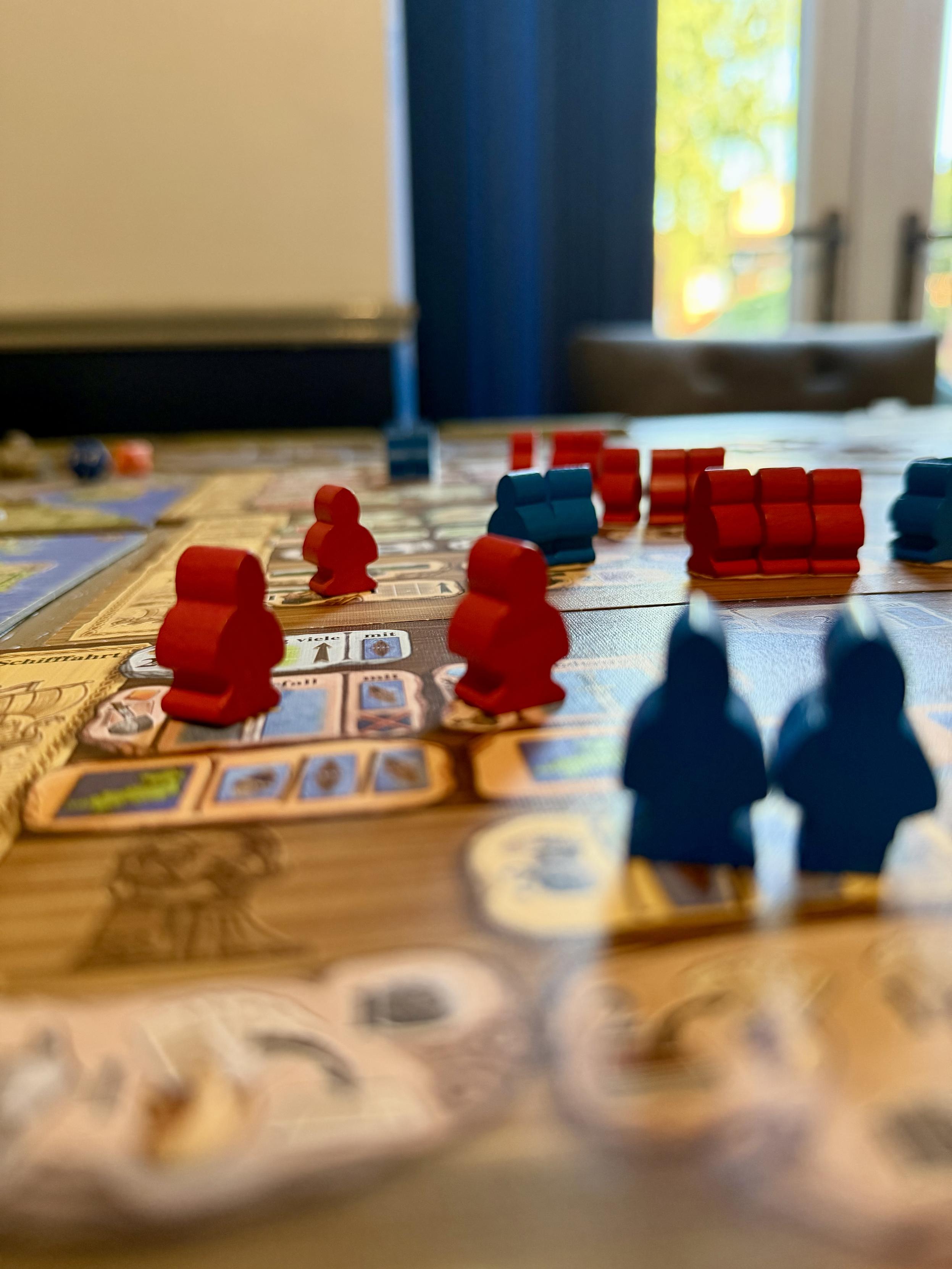 Blue and red Viking Meeples on the A Feast for Odin board. Soft focus. A view to the hot outside can be seen in the distance.