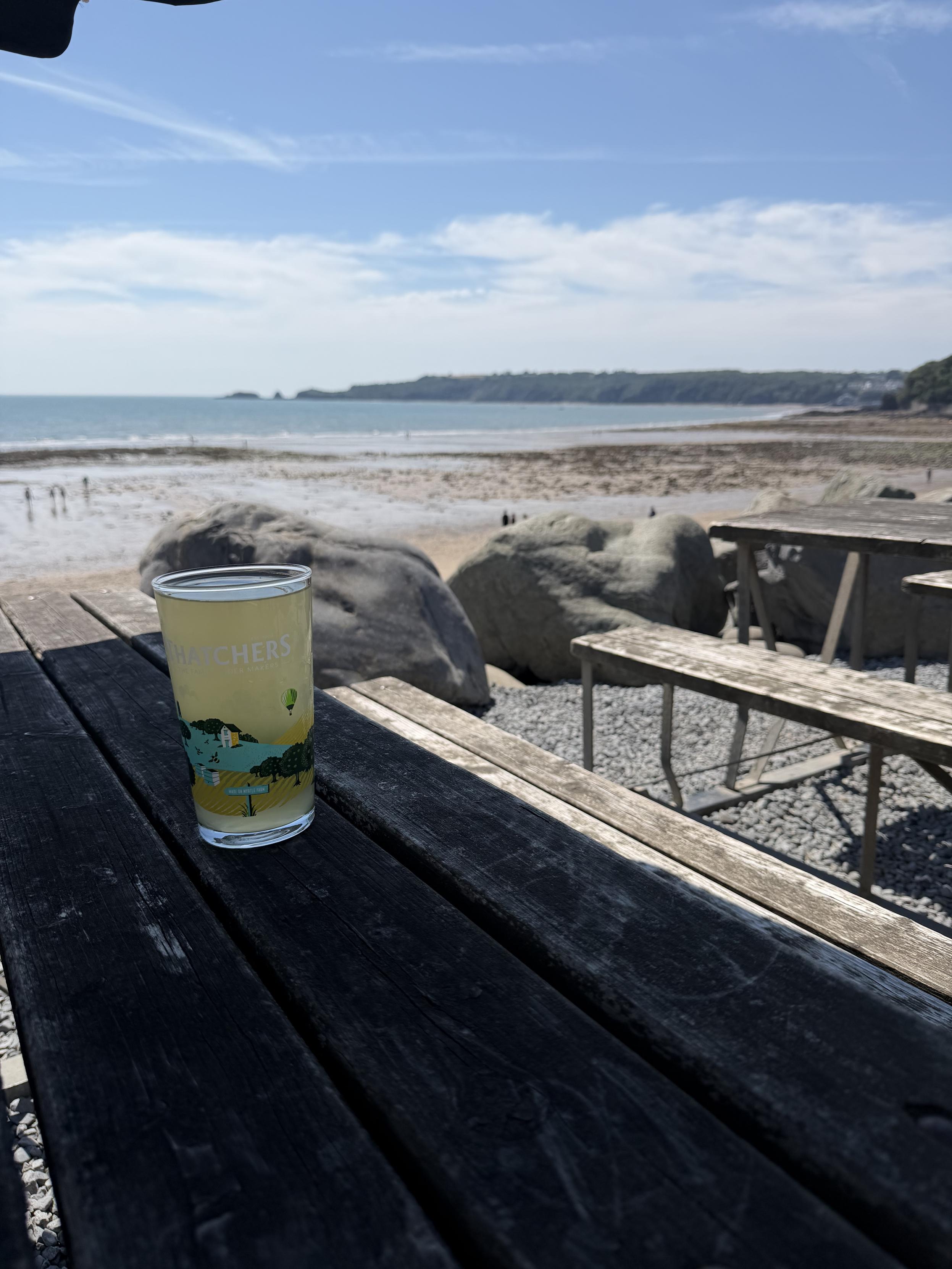 A glass of hazy cider. On a pub table. Overlooking a bay and the sea. Baking under a hot sky.