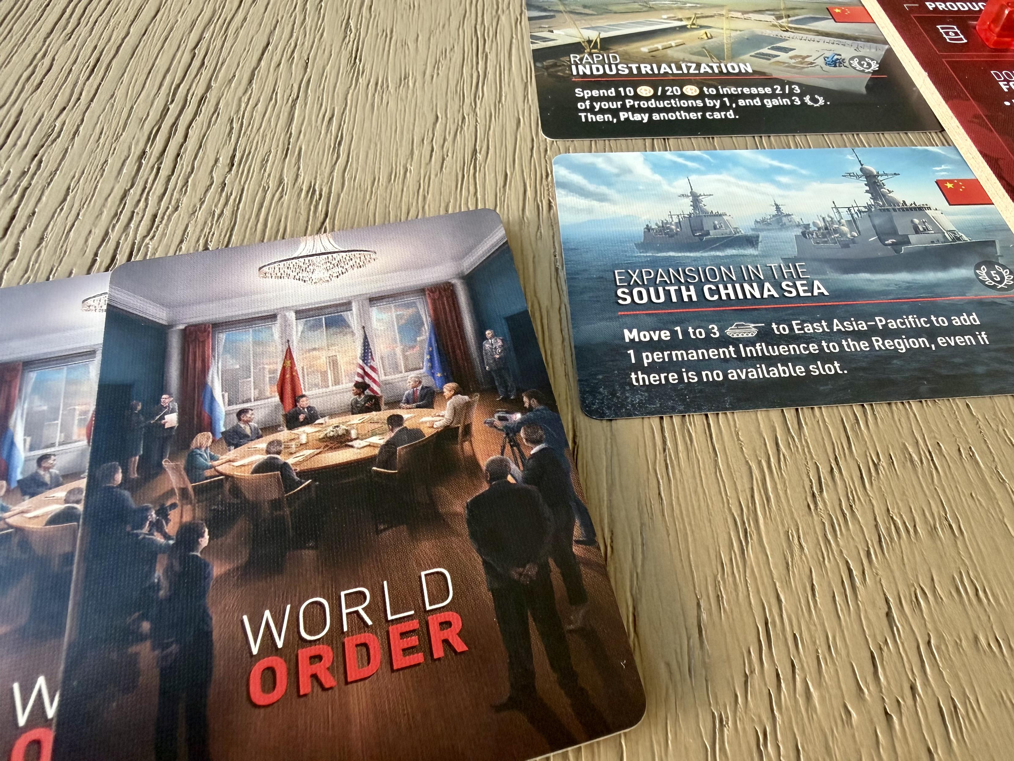 Cards for the game "World Order," featuring a meeting room and naval ships, with instructions for expansion into the South China Sea.